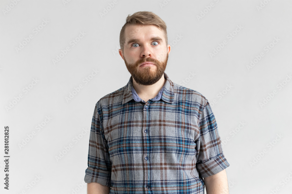 Fototapeta premium Young man with a mustache and beard making bulging eyes in surprise against a white background. Concept of surprise and uncertainty.