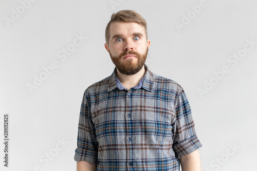 Young man with a mustache and beard making bulging eyes in surprise against a white background. Concept of surprise and uncertainty.