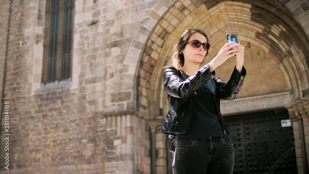 Attractive tourist woman making a selfie uses a smartfone while walking at the street.
