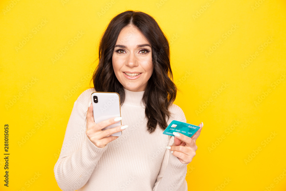 Woman in an elegant dress holding phone and credit card isolated on the yellow background Woman in an elegant dress holding phone and credit card isolated on the yellow background