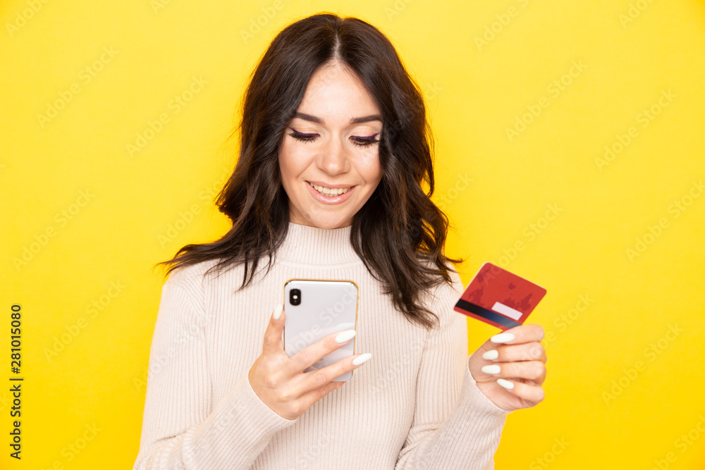 Woman in an elegant dress holding phone and credit card isolated on the yellow background Woman in an elegant dress holding phone and credit card isolated on the yellow background