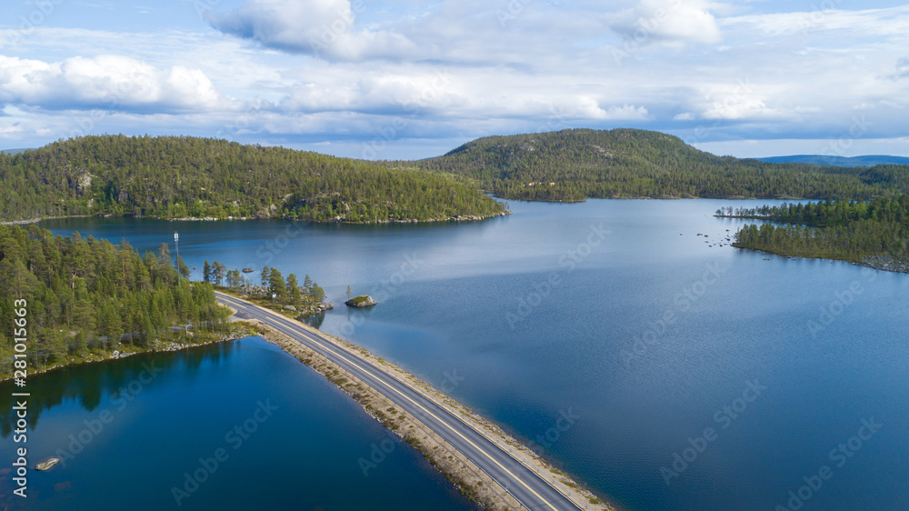 Aerial panorama of a road through forest and hills in Lapland on a cloudy day. Beautiful lake with blue water. 