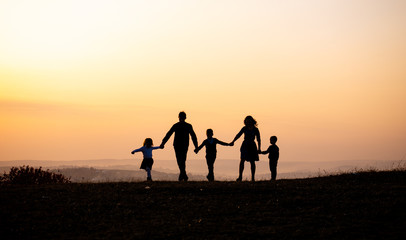 Silhouettes of happy family holding the hands in the meadow during sunset.