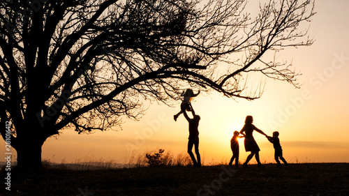 Silhouettes of family spending time together in the meadow near during sunset