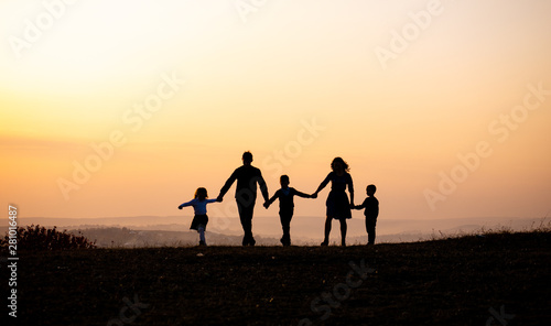 Silhouettes of happy family holding the hands in the meadow during sunset.