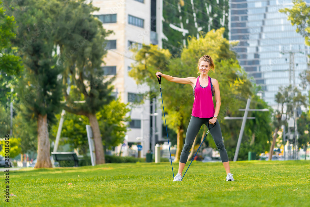 Young sportswoman performing exercises on grass in a city 