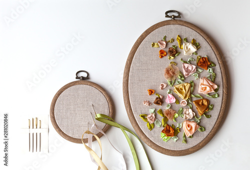 Handmade embroidery satin ribbons with flowers ornament on linen canvas in plastic hoop and special needles with a big eyelet (embroidery made by the author of the photo). Copy space, flat lay photo