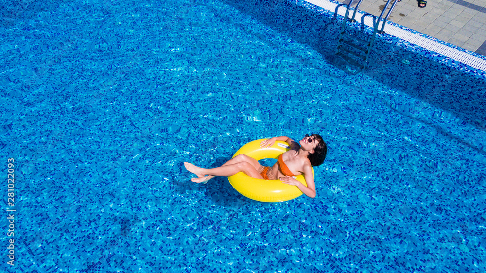 Beautiful woman relaxing on inflatable ring in blue swimming pool.