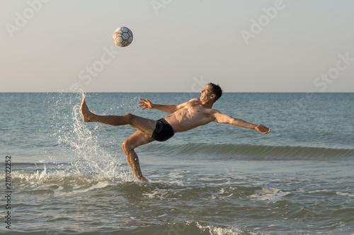 A man plays ball in the sea, kicks the ball in a jump