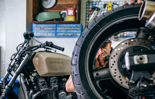 Mechanic fixing custom motorcycle wheel in his workshop. Selective focus on mechanic in background