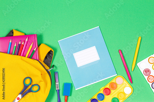 Back to school concept. Yellow backpack with school supplies and notebook on green background. Top view
