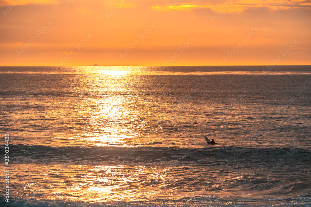 Lonely surfer is waiting for wave on beautiful sunset. Leisure, active sports concept