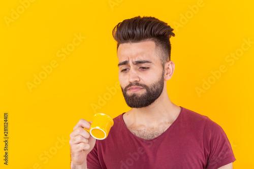Arabic man drink coffee from small cup on yellow background and he don't like it - people with coffee cup easy lifestyle concept