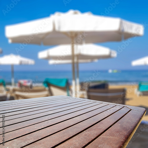 Wooden table background with sun beds and umbrellas on the beach and ocean view.
