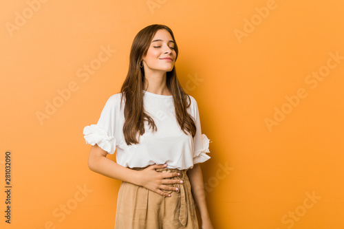 Young caucasian woman touches tummy, smiles gently, eating and satisfaction concept.