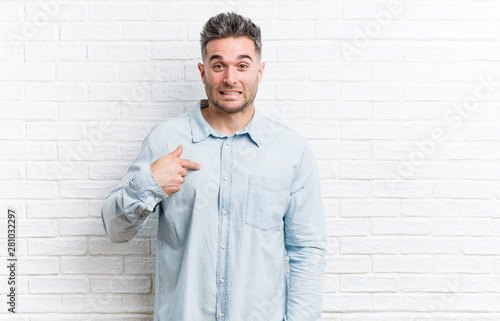 Young handsome man against a bricks wall person pointing by hand to a shirt copy space, proud and confident