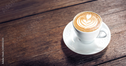 Bliska gorąca kawa cappuccino biała filiżanka z grafiką latte w kształcie serca na ciemnym brązowym starym drewnianym stole w kawiarni, koncepcja jedzenia i picia.