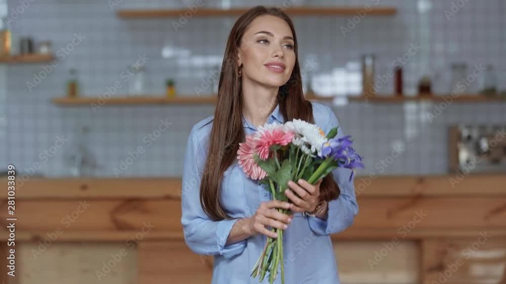 happy girl looking at camera, holding flowers, smelling and smiling at home 