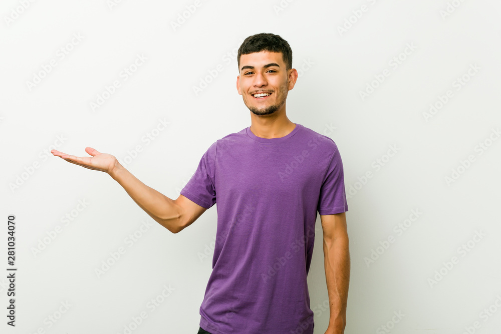 Young hispanic man showing a copy space on a palm and holding another hand on waist. Young hispanic man showing a copy space on a palm and holding another hand on waist.