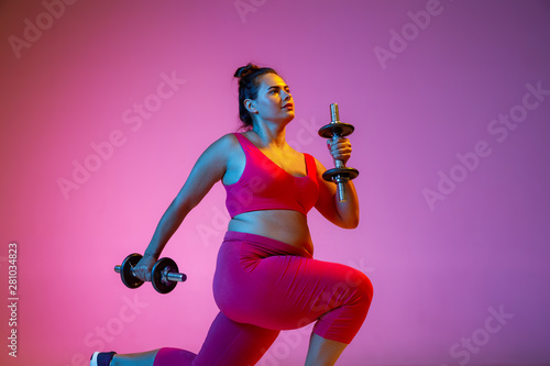Young caucasian plus size female model s doing exercises on gradient purple background in neon light. Training her upper body with the weights. Concept of sport  healthy lifestyle  body positive.