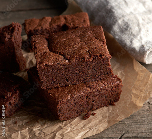 stack of baked square pieces of chocolate brownie cake on brown parchment paper
