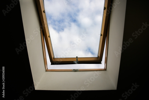 Window in the ceiling. Blue sky with clouds. Attic interior.