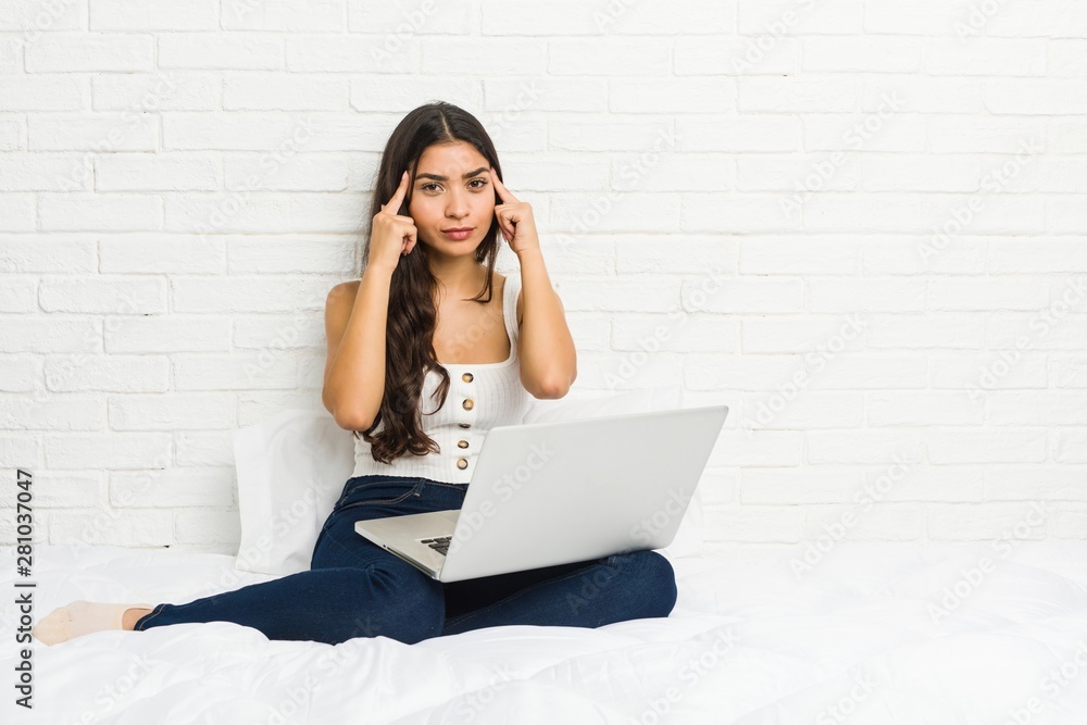 Young arab woman working with her laptop on the bed focused on a task, keeping forefingers pointing head. Young arab woman working with her laptop on the bed focused on a task, keeping forefingers pointing head.