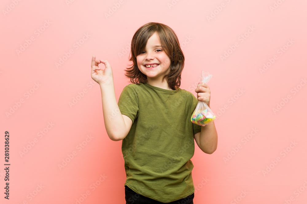 Little boy caucasian holding candies smiling cheerfully pointing with forefinger away. Little boy caucasian holding candies smiling cheerfully pointing with forefinger away.