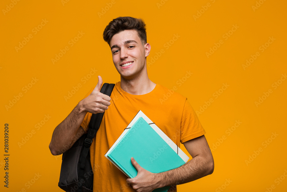Young student man holding books showing victory sign and smiling broadly. Young student man holding books showing victory sign and smiling broadly.