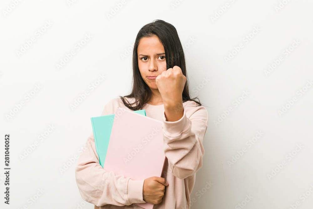 Young hispanic woman holding some notebooks showing fist to camera, aggressive facial expression. Young hispanic woman holding some notebooks showing fist to camera, aggressive facial expression.