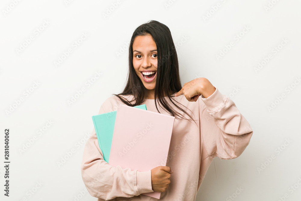 Naklejka premium Young hispanic woman holding some notebooks surprised pointing at himself, smiling broadly.