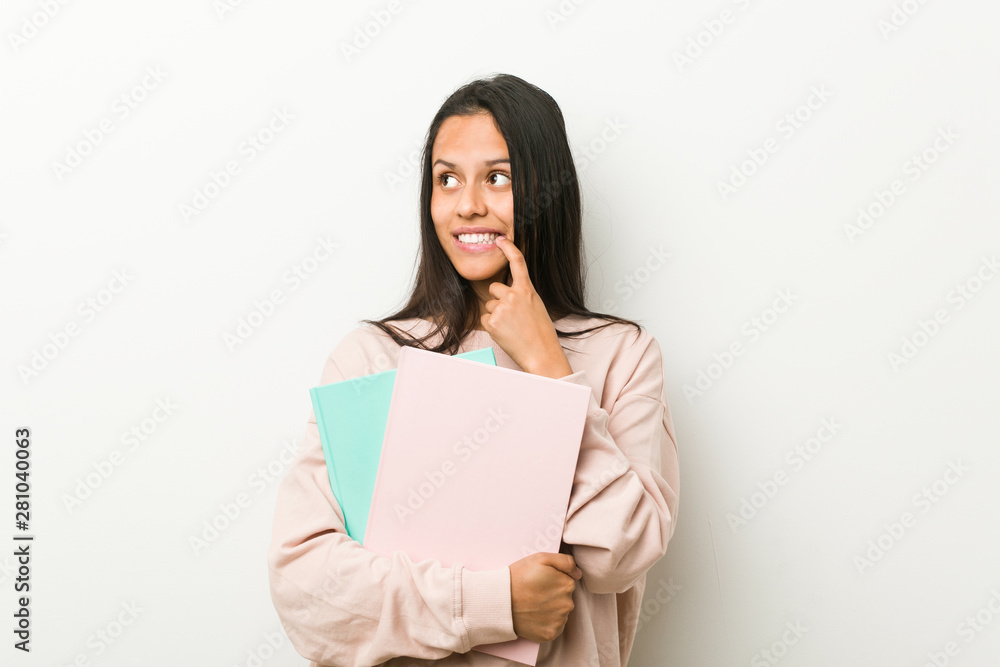 Young hispanic woman holding some notebooks relaxed thinking about something looking at a copy space. Young hispanic woman holding some notebooks relaxed thinking about something looking at a copy space.
