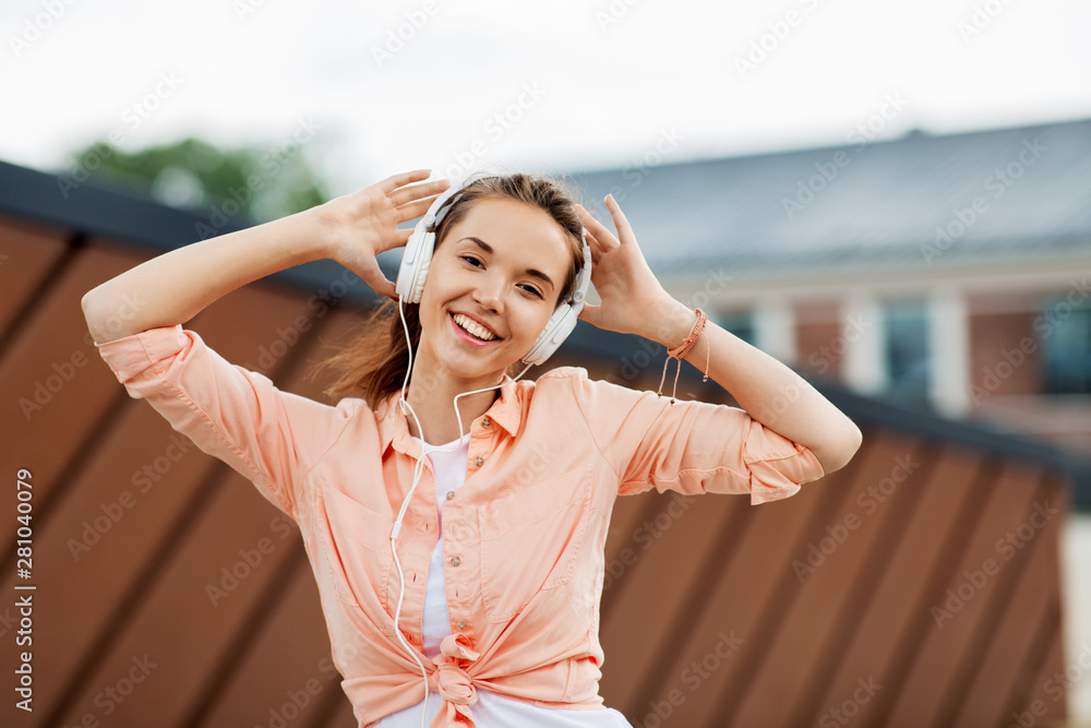 music, summer and leisure concept - happy teenage girl with headphones in city