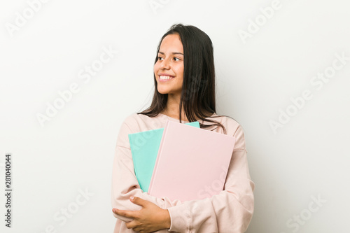 Young hispanic woman holding some notebooks smiling confident with crossed arms.