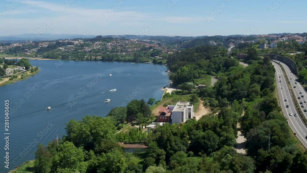 At center, a corridor of trees paints the image in green, sided by a busy road and the Douro River in Oporto (Portugal). Zoom in to the river with a few boats. Urban portrait in the background. At center, a corridor of trees paints the image in green, sided by a busy road and the Douro River in Oporto (Portugal). Zoom in to the river with a few boats. Urban portrait in the background.