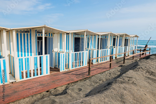 Beautiful sea  the black sandy beach and white and blue striped beach houses  Tyrrhenian sea near Roma  Italy