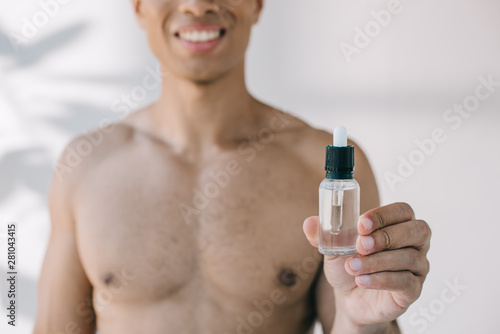 selective focus of muscular mixed race man showing bottle with serum to camera