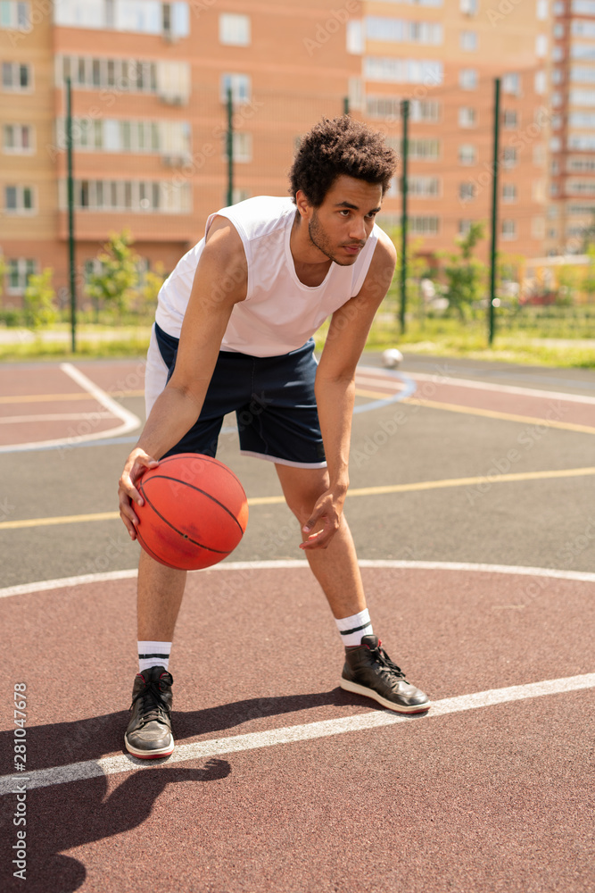 Young basketballer in activewear bending forwards before throwing ball