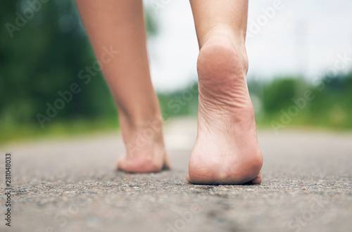 Close up of the young girl's bare feet walking along asphalt road .Rear very low angle view. © Georgy Dzyura