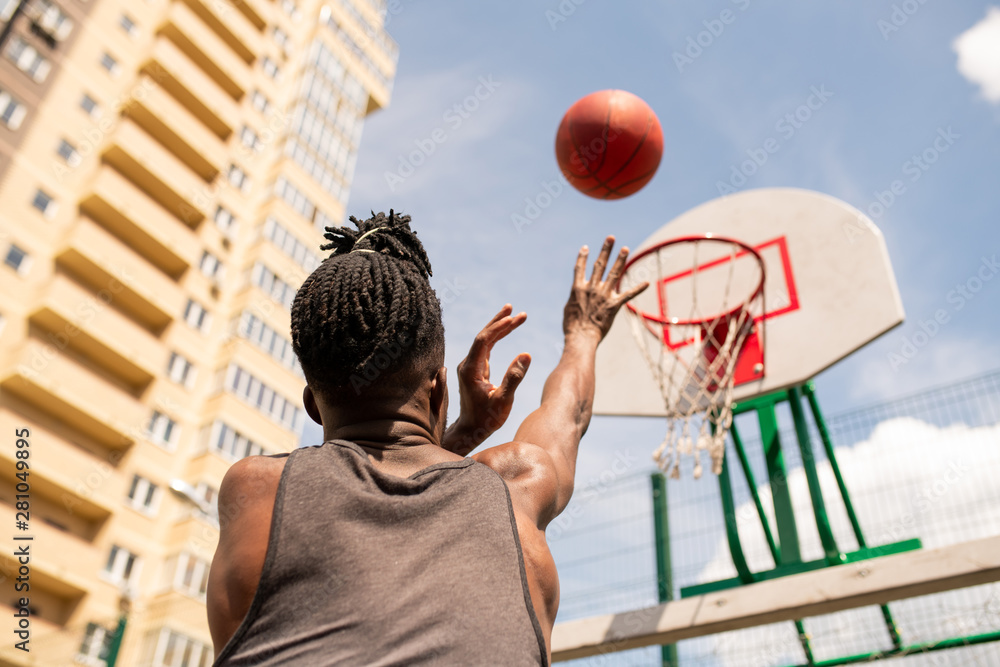 Fototapeta premium Rear view of young African basketball player throwing ball in basket