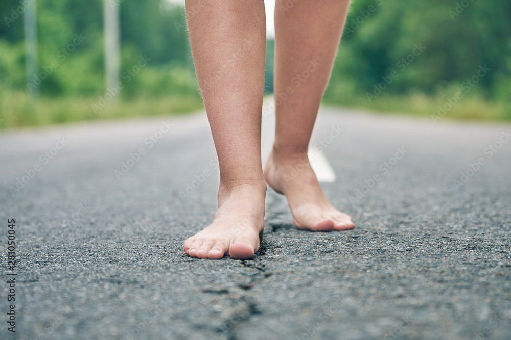 Bare feet of a young girl walking along the asphalt road