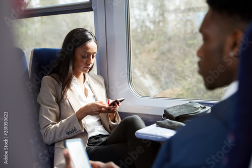 Business Passengers Sitting In Train Commuting To Work Looking At Mobile Phones