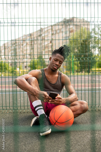 Restful African guy in sportswear scrolling or texting in smartphone © pressmaster