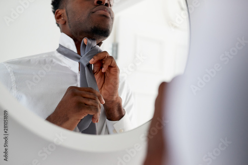 Fotografie Businessman At Home Tying Necktie In Mirror Before Leaving For Work
