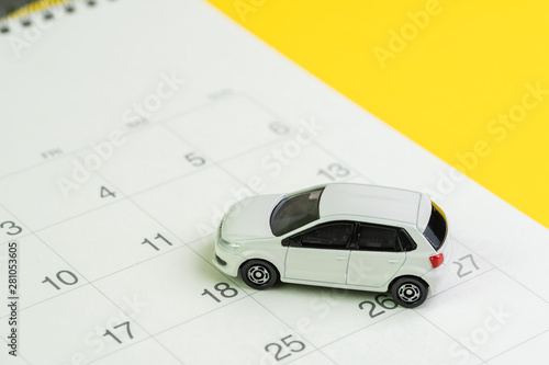 Car loan payment, buying new car or yearly maintenance schedule concept, miniature white car on clean calendar with date on yellow background
