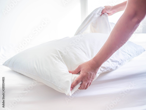 White pillow on the bed in the bedroom with woman 's hand who are making the room.
