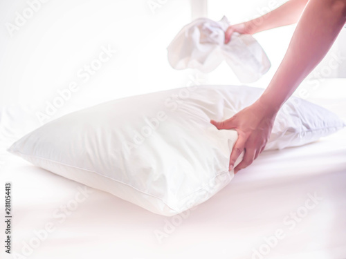 White pillow on the bed in the bedroom with woman 's hand who are making the room.