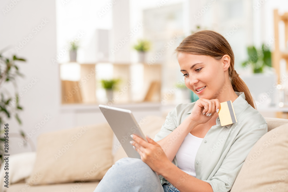 Pretty girl with touchpad and plastic card looking through goods in online shop Pretty girl with touchpad and plastic card looking through goods in online shop