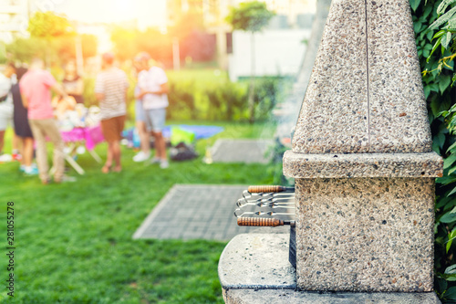 Outdoor stone stove with grill and skewers. Company of friends at barbecue party at park or backyard with green grass lawn and brazier. People having fun cooking food during bbq weekend at garden photo