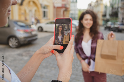 Cropped close up of a smart phone in the hands of a woman taking photo of her friend on the city streets. Female friends enjoying sightseeing and taking photos after shopping